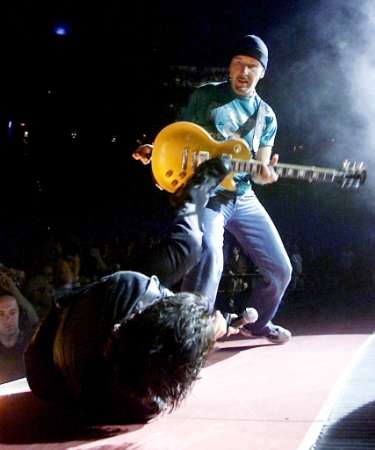 U2 singer Bono (L) kicks The Edge's guitar during a sold-out stop of the band's Elevation Tour at the Thomas & Mack Center in Las Vegas November 18, 2001. The band is touring to support the album "All That You Can't Leave Behind." REUTERS Ethan Miller/Las Vegas Sun