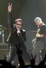 U2 lead singer Bono, left, flashes a peace sign as he sings as Adam Clayton, right, plays behind him during the first concert of their Vertigo Tour at the San Diego Sports Arena Monday, March 28, 2005. (AP Photo/Denis Poroy)