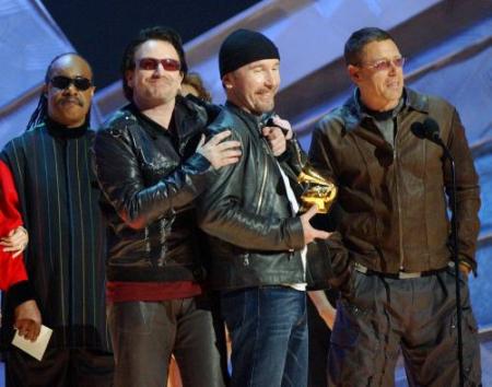Bono, of U2, second left, embraces The Edge as they accept the Grammy for record of the year along with Adam Clayton, right, during the 44th annual Grammy Awards, Wednesday, Feb. 27, 2002, in Los Angeles. At far left is presenter Stevie Wonder. (AP Photo/Kevork Djansezian)